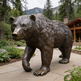Bronze bear statue in front of a wooden cabin with mountains in the background