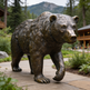 Bronze bear statue in a natural setting with trees and a building in the background