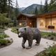 Statue of a bear in front of a modern wooden cabin with mountains in the background
