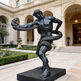 Statue of a muscular figure holding a snake in front of an elegant building with arches and columns.