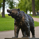 Bronze bear statue in a park setting with green grass and trees.