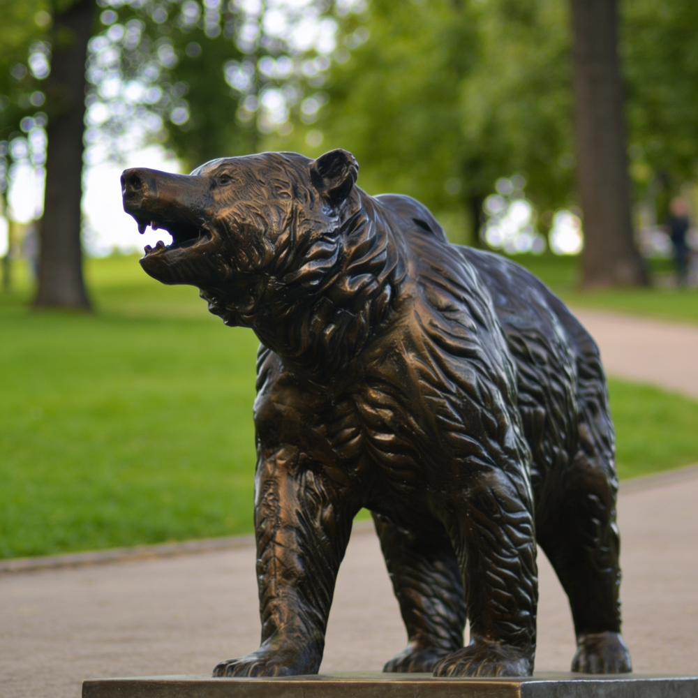 Bronze bear statue in a park setting with green grass and trees.