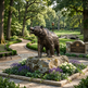 Bronze bear statue on a rock in a park setting with flowers and a bench.