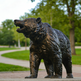 Bronze bear statue in a park setting with trees and grass.