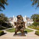 Bronze bear statue in front of a large house with a clear blue sky.