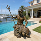 Bronze statue of a bearded man with a trident on a turtle by a poolside.