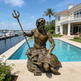 Bronze statue of a mythological figure by a pool with a house and marina in the background