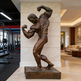 Bronze statue of a muscular figure in a gym setting