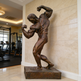 Bronze statue of a muscular figure in a gym setting