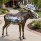 Metallic moose statue with reflective surface in a garden setting