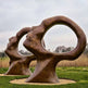 Large abstract bronze sculpture in a park setting with grass and trees in the background