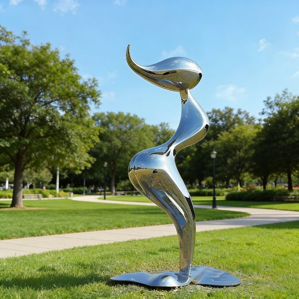 Silver abstract sculpture in a park with green grass and trees.