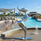 Metallic sculpture by a pool with children playing in the background