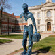 Blue metal statue of a person with a suitcase in front of a building