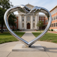 Contemporary heart‑form sculpture made of metal, with two hands joining at the upper point