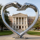 Large metallic heart sculpture with interlocking hands, installed in front of a classical columned building.