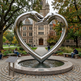Modern symbolic sculpture of a heart formed by two hands, mounted on a pedestal in an institutional setting