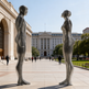 Two metallic sculptures of human figures in a public square with a building in the background.