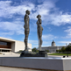 Reflective sculpture of two abstract figures created from stacked circular metal layers.