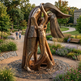 Bronze sculpture of two people embracing in a park setting with greenery and flowers.
Reflective metal sculpture showing a stylized couple embracing with angular detailing