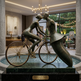 Bronze sculpture of two people on a bicycle in an indoor setting with decorative lighting and decor.