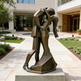 Bronze sculpture of a couple embracing in an outdoor setting with a building in the background