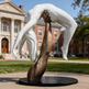 Bronze sculpture of an upright arm holding a suspended white human figure in an arched pose.