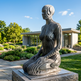 Modern sculpture in a garden setting with a building and trees in the background
