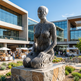 Modern sculpture in front of a building with people and outdoor seating area