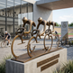 Bronze sculpture of cyclists in a line outside a building with bicycles in the background.