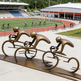 Bronze sculpture of cyclists in a line at a track and field stadium