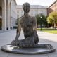 Modern metal artwork featuring a seated figure formed from thin vertical layers.