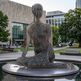 Modern sculpture of a seated figure in an urban park setting with buildings and trees in the 
background.
Industrial‑style sculpture of a human silhouette built from stacked metal strips