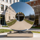 Reflective metal sculpture in an outdoor setting with buildings in the background
Reflective circular sculpture featuring a smooth central hole