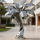 Reflective metal palm tree sculpture with smooth curved leaves and a spiral‑shaped trunk