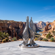 Metallic sculpture in a desert setting with mountains and a river in the background