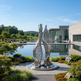 Modern sculpture in a garden setting with a building and pool in the background