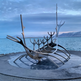Modern polished metal sculpture resembling a Viking ship with upward‑reaching curved forms