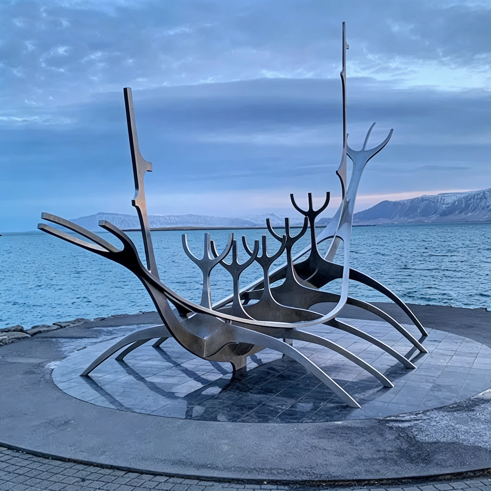 Modern polished metal sculpture resembling a Viking ship with upward‑reaching curved forms