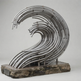 A wave-shaped metal sculpture made of curved silver tubes mounted on a rough stone base, photographed against a plain light gray studio background.