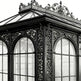 Ornate glass conservatory with intricate metalwork on a white background