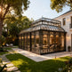 Orangery attached to a house with decorative glass roof and walls, surrounded by trees and garden.