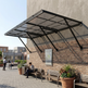Outdoor awning attached to a building wall with people sitting on benches below.