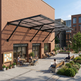 Outdoor seating area with people at tables and on benches in front of a brick building with a canopy.