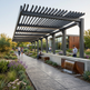 Patio with pergola, water feature, and people walking in a garden setting