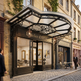 Luxury store front with decorative canopy and 'L'Atelier d'Artiste' sign on a cobbled street.