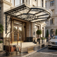 Luxury hotel entrance with decorative canopy, luggage cart, and car in front.