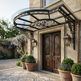 Decorative metal canopy over a wooden door with potted plants and a garden view.
