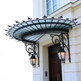 Wrought iron scrollwork canopy installed above double wooden door.
