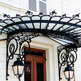 Curved glass awning with heavy wrought iron brackets and decorative scroll patterns.
